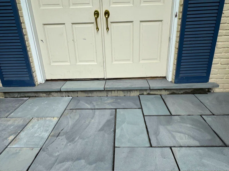 Close-up of gray stone threshold pieces installed at front entry doors during porch resurfacing project