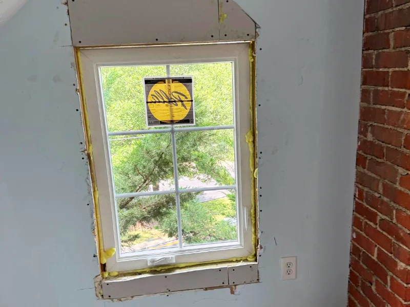 New casement window installed with insulation foam visible around the frame before drywall and trim repairs were completed.