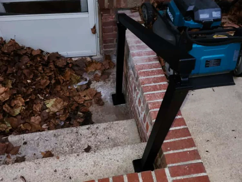 A newly installed black wrought iron handrail tracking down a concrete basement staircase at a forty-five-degree angle next to a red brick retaining wall.