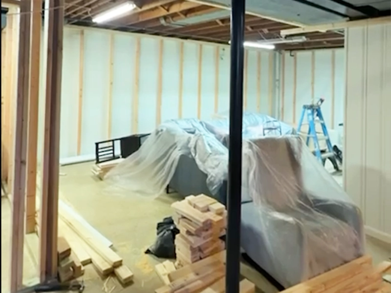 Basement framing in progress with construction materials, layout markings, and walls prepared for drywall installation.