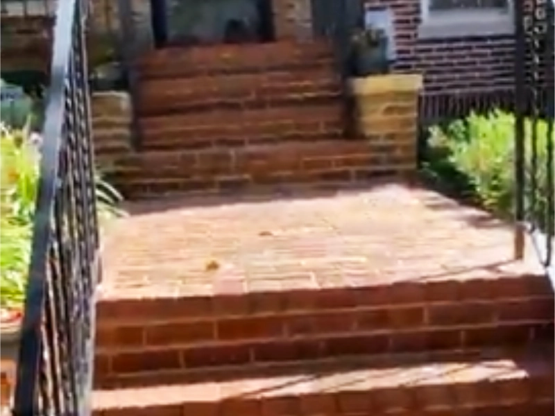 A front view of a brick home entrance and staircase showing weathered, deteriorating mortar joints and failing spot repairs across the steps and landings prior to a complete masonry restoration.