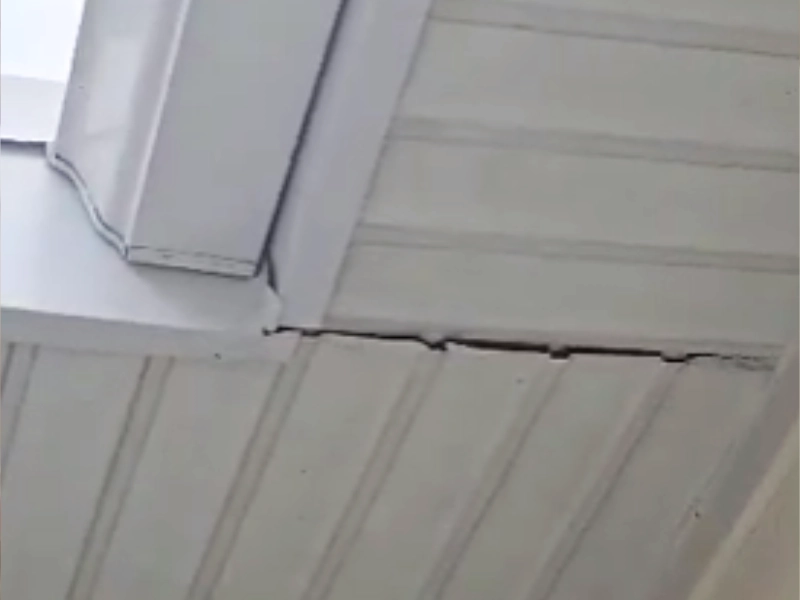 A detailed view looking up at a significant crack where the white exterior soffit siding meets a corner trim piece before being sealed.