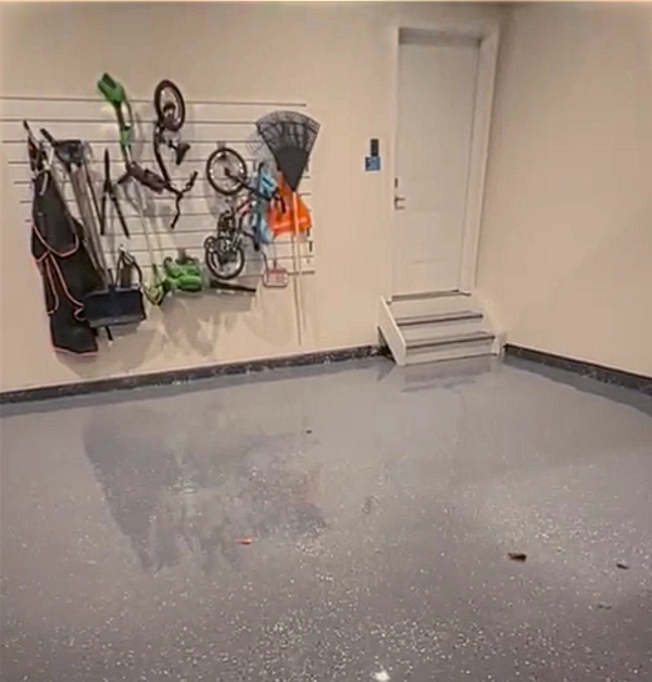 A freshly renovated garage showcases a seamless, glossy gray epoxy floor coating embedded with decorative flakes that creates a highly reflective, clean surface.