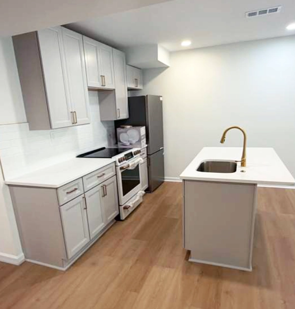 Completed basement in-law suite featuring a modern kitchen with a center island, quartz countertops, gray cabinetry, recessed lighting, and an open living area.