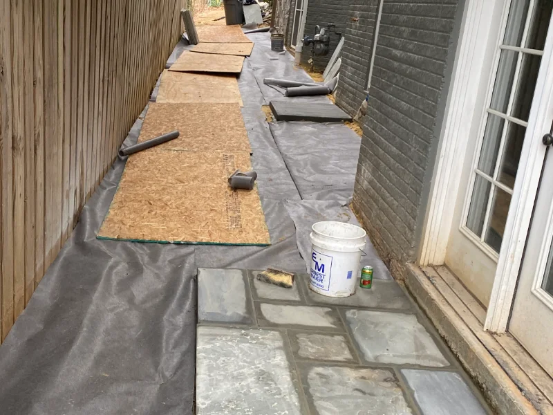 Natural flagstone being installed over the prepared base while the surrounding river rock drainage bed is completed.