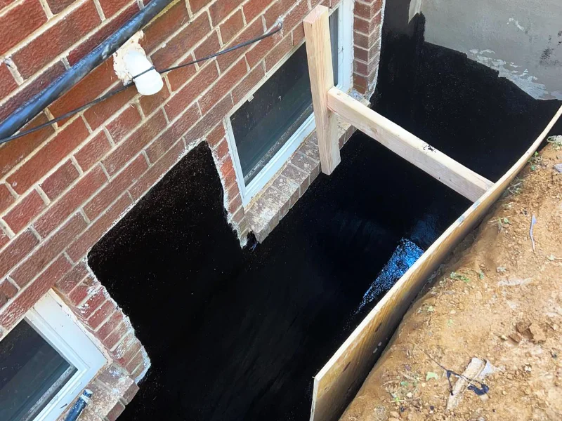 Foundation wall coated with waterproofing material and protected by a drainage membrane before backfilling and final grading.
