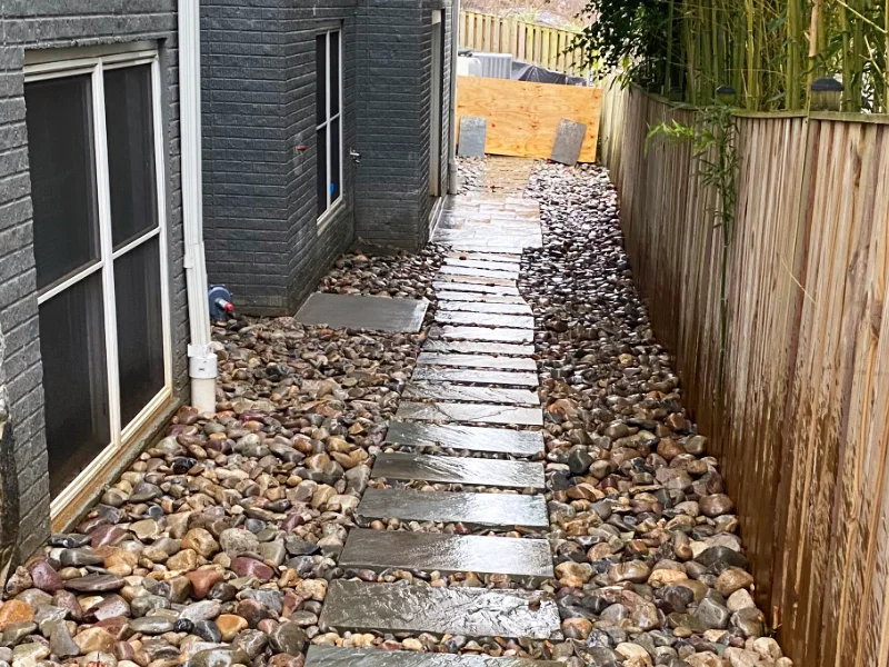 River rock drainage installation surrounding the foundation with the downspout directed into the stone bed.