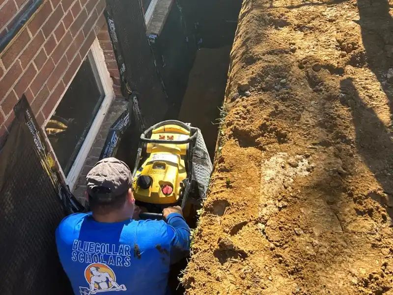 Crew member working inside a deep excavation trench while preparing the exposed foundation wall for crack repair and waterproofing membrane installation.