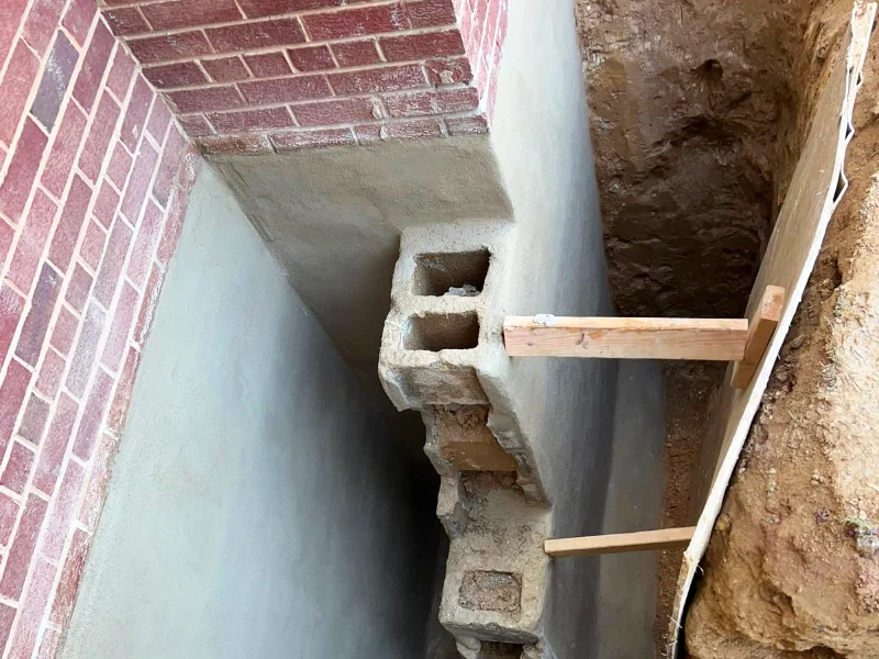 Exposed foundation wall after surface repairs and preparation for exterior waterproofing treatment.