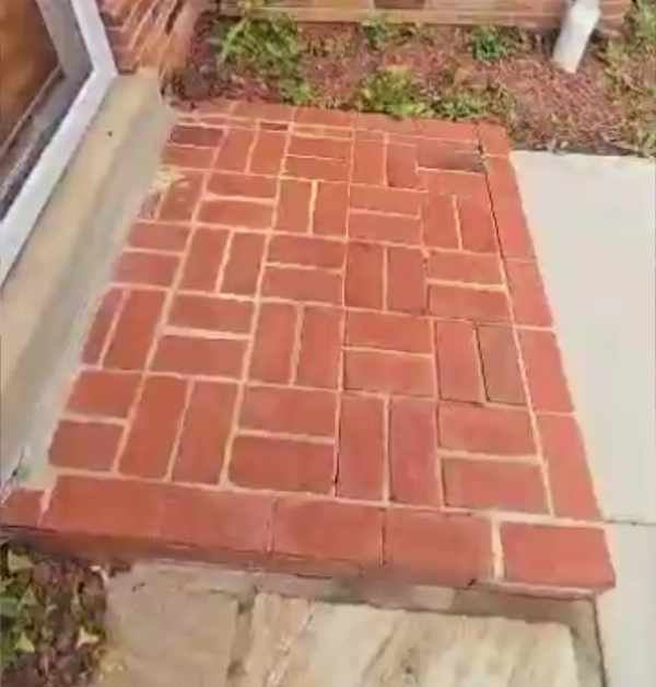 A detailed perspective view showing the sleek black wrought iron handrail installed on the side of the raised red brick landing next to the front entrance door.