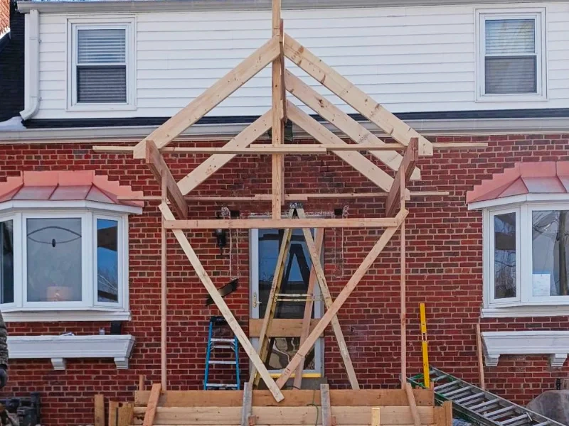 An exterior home construction shot showing the complete raw wood structural skeleton of a new gabled portico roof built over the front door.