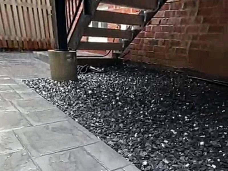 Gravel drainage area beneath the rear porch connected to a stamped concrete landing and patio, creating a clean transition from the stairs to the backyard.