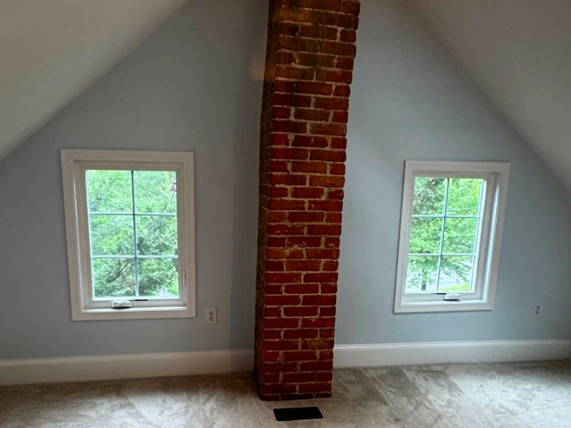 Finished attic room with restored walls, exposed brick chimney, and newly installed casement egress windows.