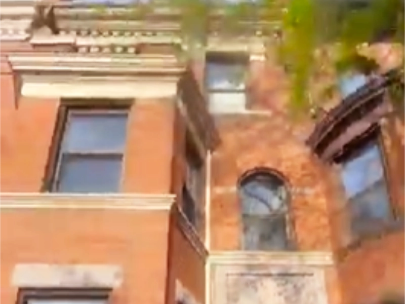 A low-angle view of a historic red brick rowhouse before renovation, showing weathered masonry, faded brown trim, and an unpolished entrance.