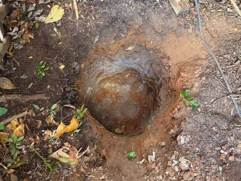 Deep excavation for a new porch footing exposing clay soil and a large buried rock before concrete placement.