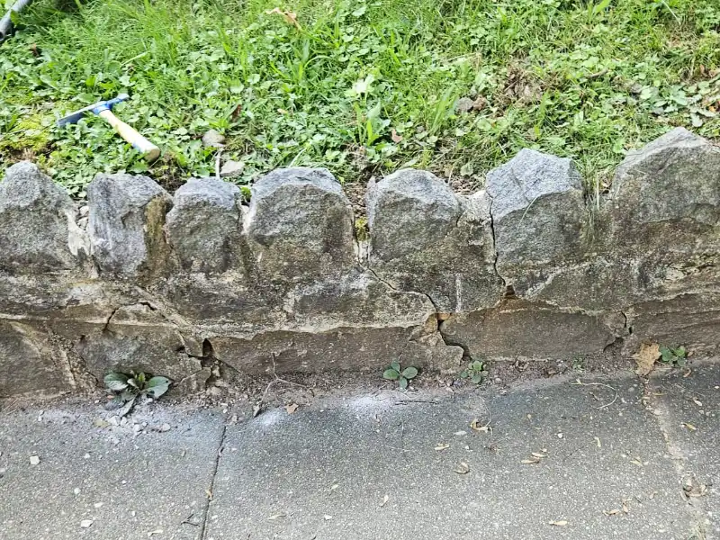 Aging leaning retaining wall along a residential sidewalk showing deteriorated mortar joints, loose masonry, and sections requiring repair before restoration work began.