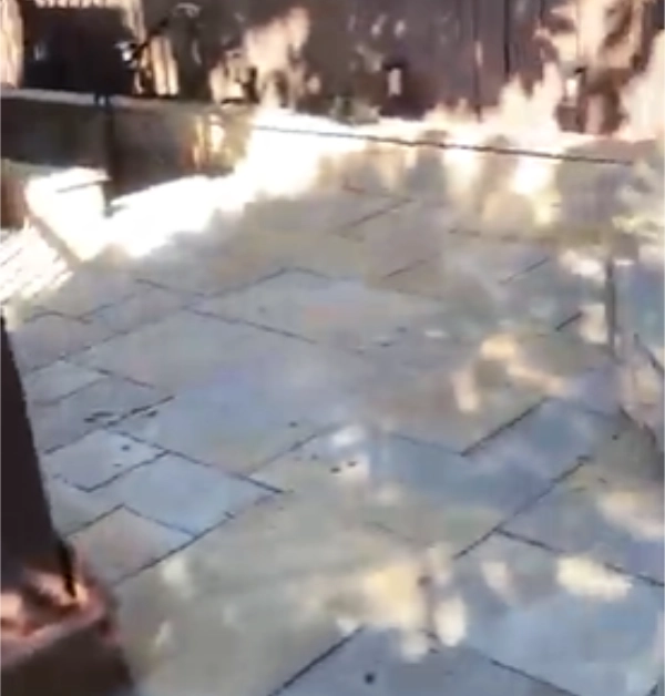A sun-lit, wide view of an eighteen-by-fifteen-foot flagstone patio prior to restoration, showing weathered joints where the original polymeric sand has begun washing out.