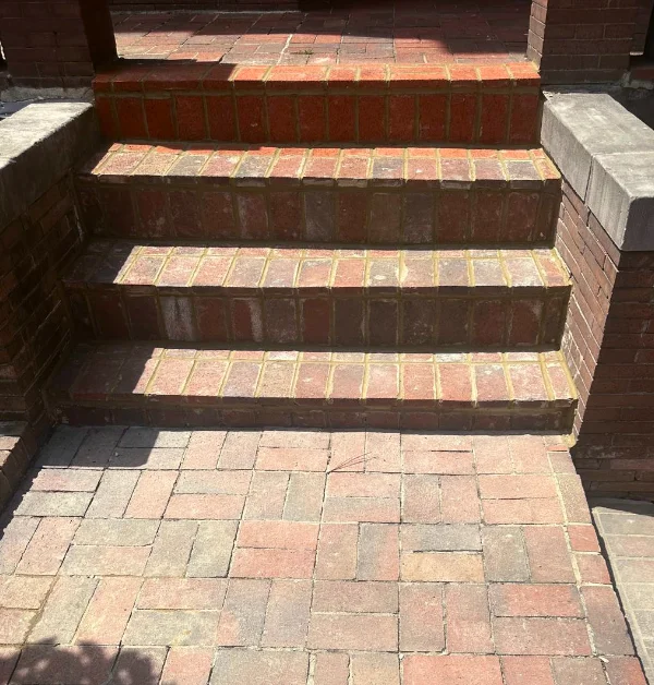 A clean, freshly repointed brick staircase and matching brick paver walkway illuminated by bright sunlight and sharp tree shadows.