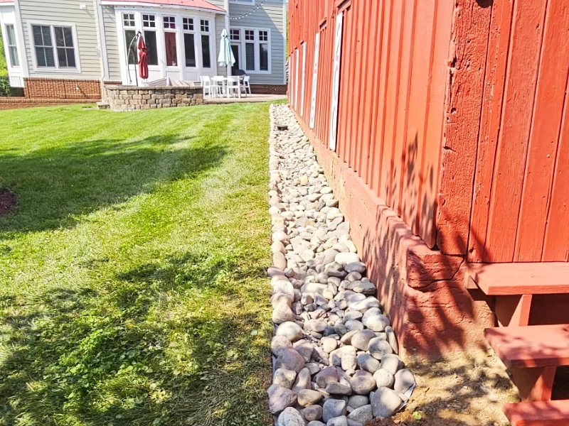 Decorative river gravel placed over the drainage system to promote water infiltration while protecting the underground pipe network.