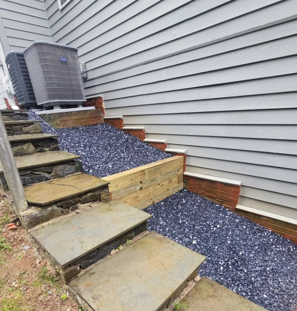 A stabilized residential HVAC condenser unit sits securely atop a newly constructed timber retaining platform filled with dark gravel.
