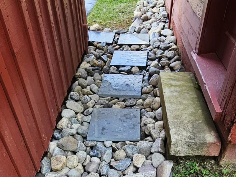 Finished stepping stone walkway integrated into the drainage system between two historic barn structures.