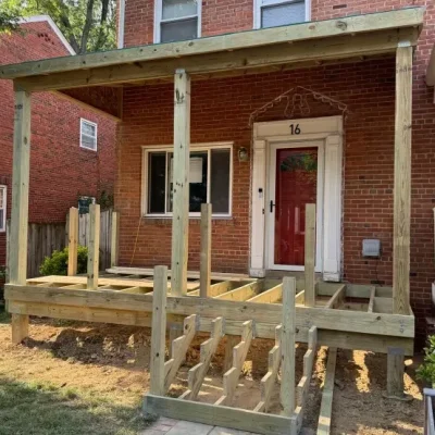 Construction of a wooden porch structure in front of a brick house.