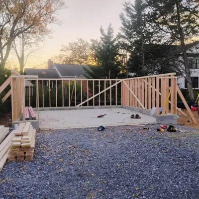 Framed structure under construction with wooden beams on a gravel lot at sunset.